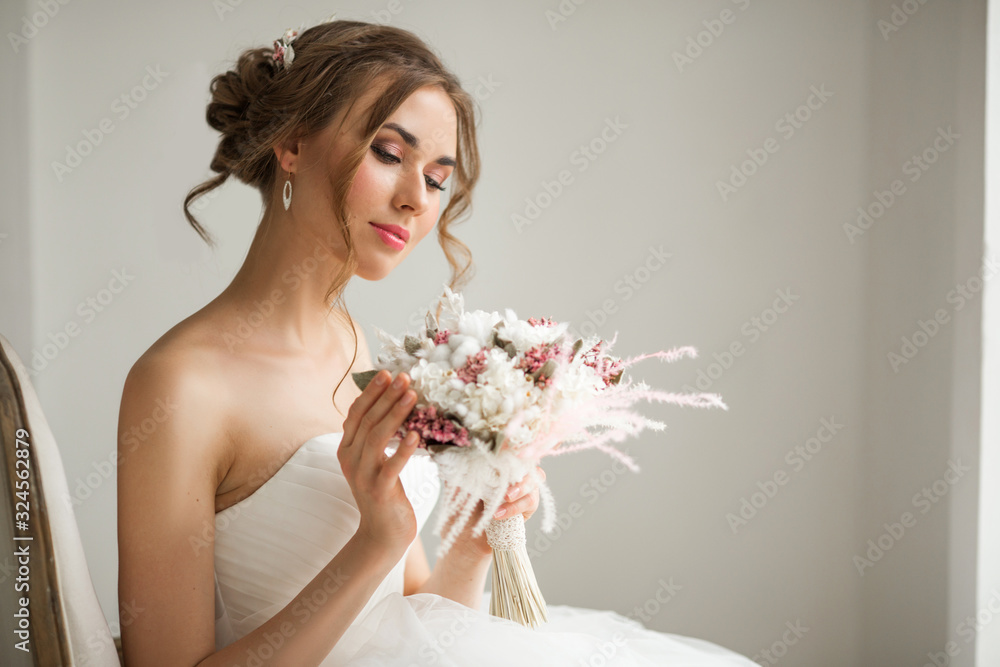 Close up portrait of young bride in a beautiful dress holding a bouquet of flowers in bright white studio. Wedding concept.