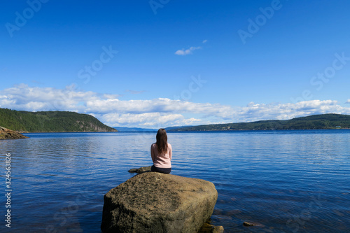 Beautiful young woman sitting in peace on a rock contemplating the Saguenay fjord 