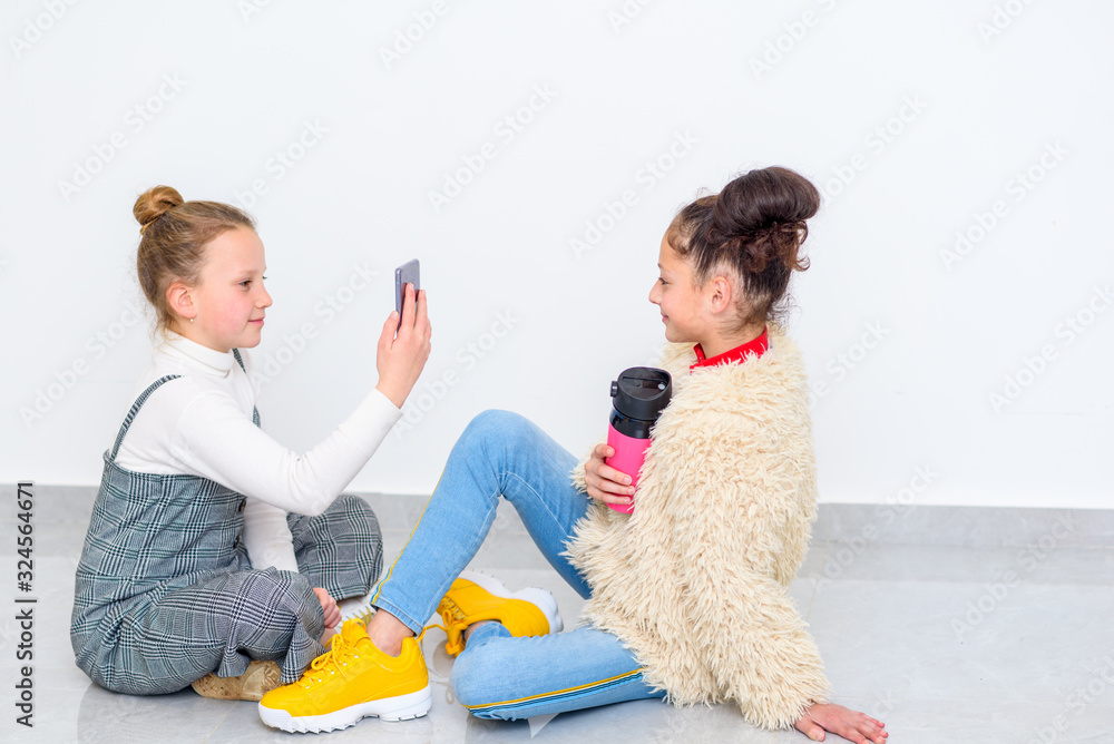 Close up portrait of two diverse teen girls. Youth woman uses smart phone to take portrait of black hair teenage drinking hot coffee from reusable pink cup. Close up portrait of two diverse teen girls. Youth woman uses smart phone to take portrait of black hair teenage drinking hot coffee from reusable pink cup.