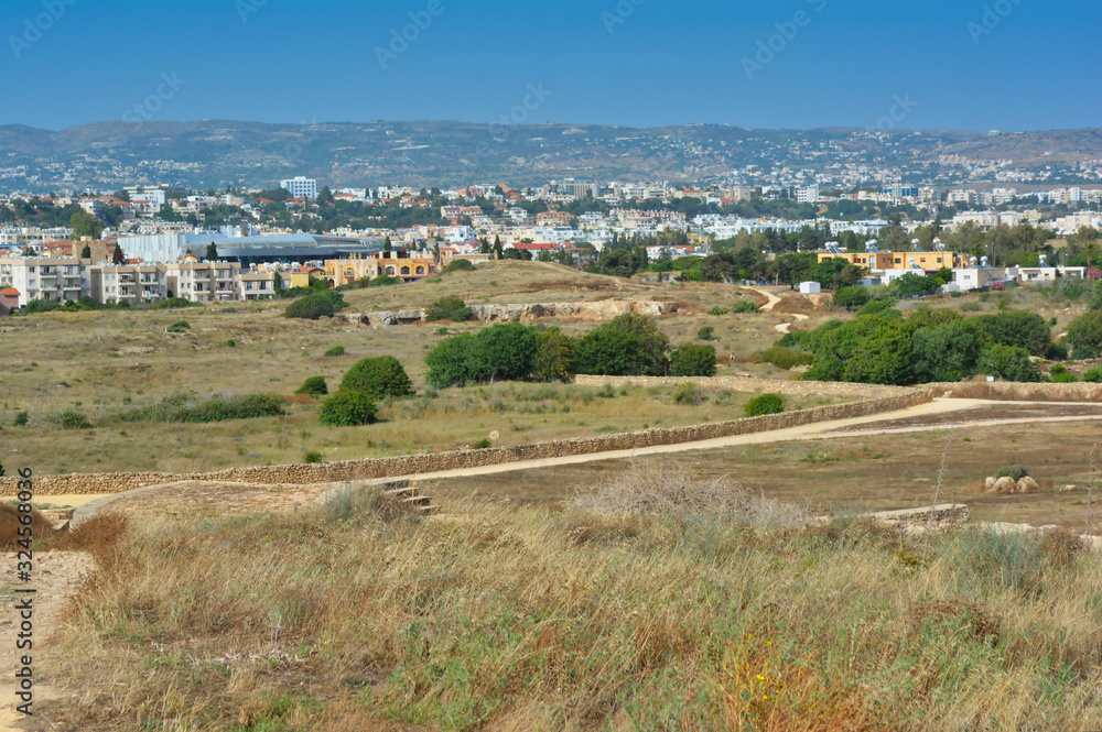 view of the city and mountains, opening from a plain with grass and green trees against a cloudless blue sky