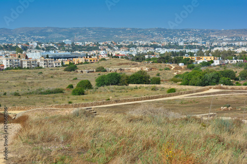 view of the city and mountains, opening from a plain with grass and green trees against a cloudless blue sky