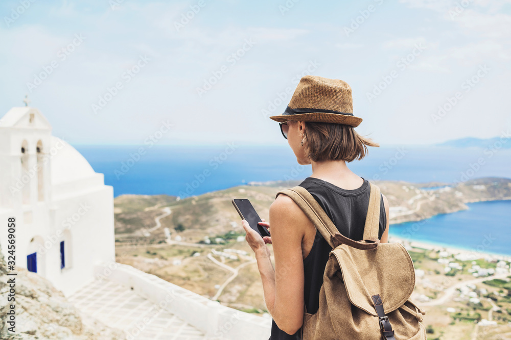 Young tourist woman using smartphone over beautiful landscape with sea in Greece. Traveler girl with backpack and mobile phone. Travel, tourism, summer holidays, active lifestyle concept