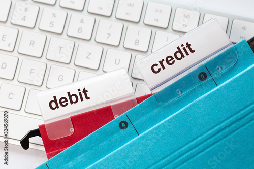 tow hanging folders on in red and in blue on a keyboard having tabs with the words debit and credit on it