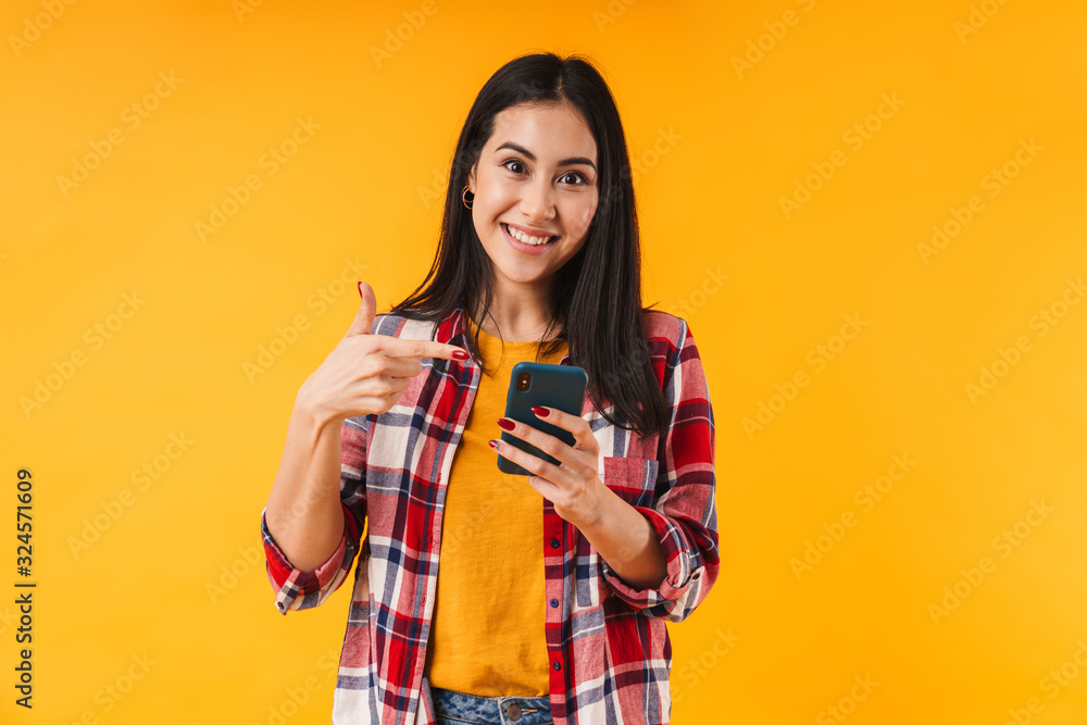 Photo of pleased brunette woman holding and pointing finger at cellphone Photo of pleased brunette woman holding and pointing finger at cellphone
