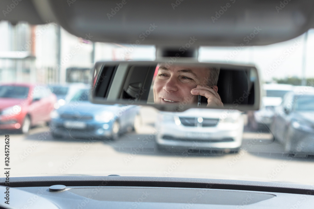Reflection of face of middle aged man talking on a mobile phone and laughing in the car rear view mirror. Reflection of face of middle aged man talking on a mobile phone and laughing in the car rear view mirror.