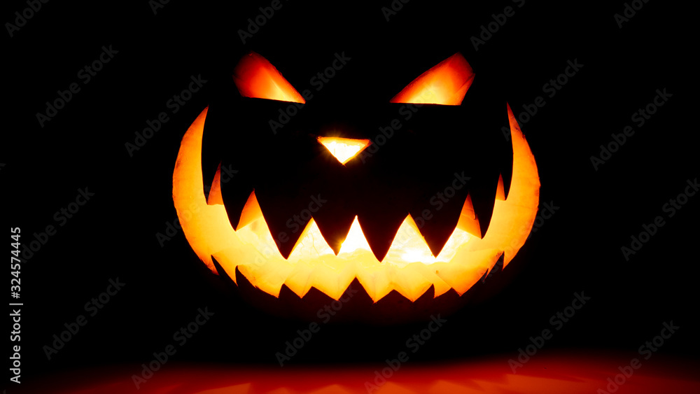 Naklejka premium Scary face halloween pumpkin on a black background. Luminous smiling glowing face