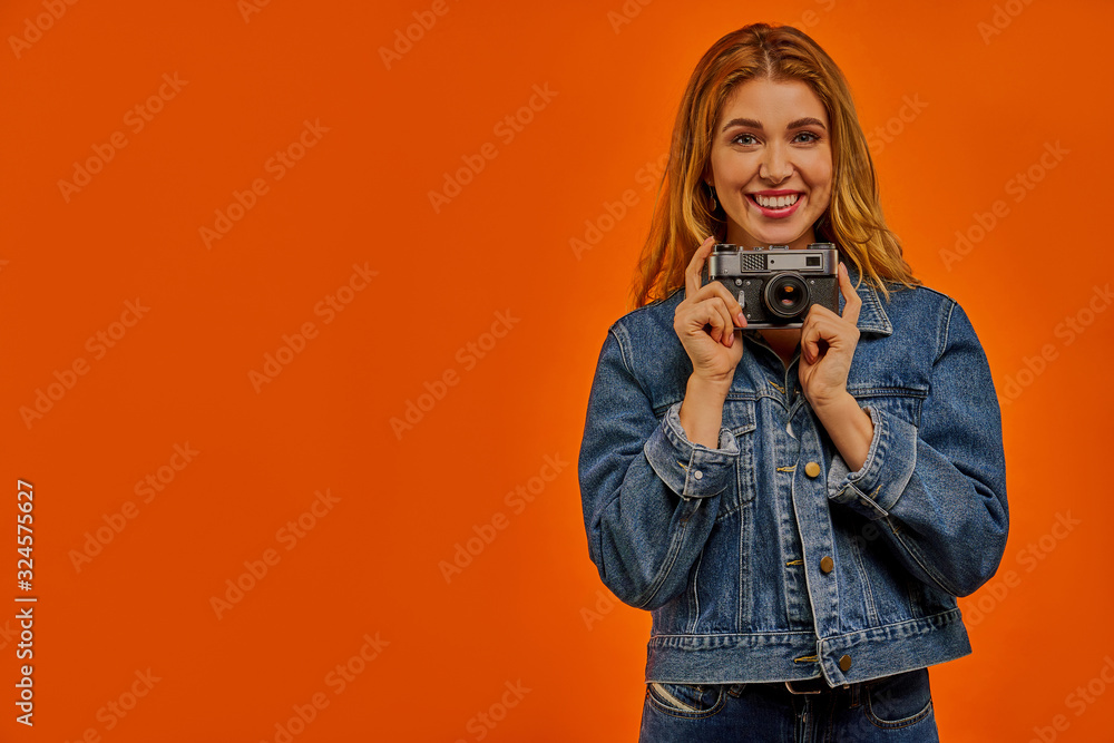 Smiling woman with wavy hair in a denim jacket holds a photo camera. Smiling woman with wavy hair in a denim jacket holds a photo camera.