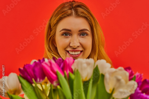 Happy girl with short loose hair receives a bouquet of white and purple tulips as a gift.