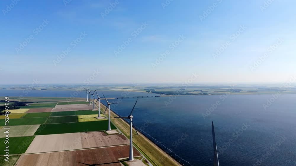 Aerial view of windmill turbines line with rotating propeller standing in area of coastline and farmland agri meadow. Generating renewable energy for clean resources. Electricity power eco production Aerial view of windmill turbines line with rotating propeller standing in area of coastline and farmland agri meadow. Generating renewable energy for clean resources. Electricity power eco production