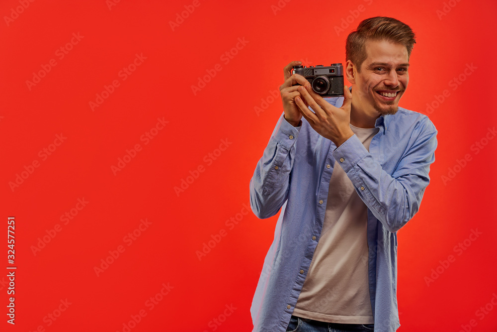 Joking man with a beard in a blue shirt holding an old photo camera to take a photo. Joking man with a beard in a blue shirt holding an old photo camera to take a photo.