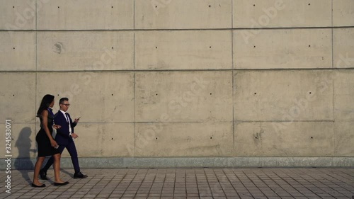 Wallpaper Mural Full length view of two successful business people walking on city street and communicating with each other. Women and men colleagues using mobile phones  passing wall with copy space area for text Torontodigital.ca