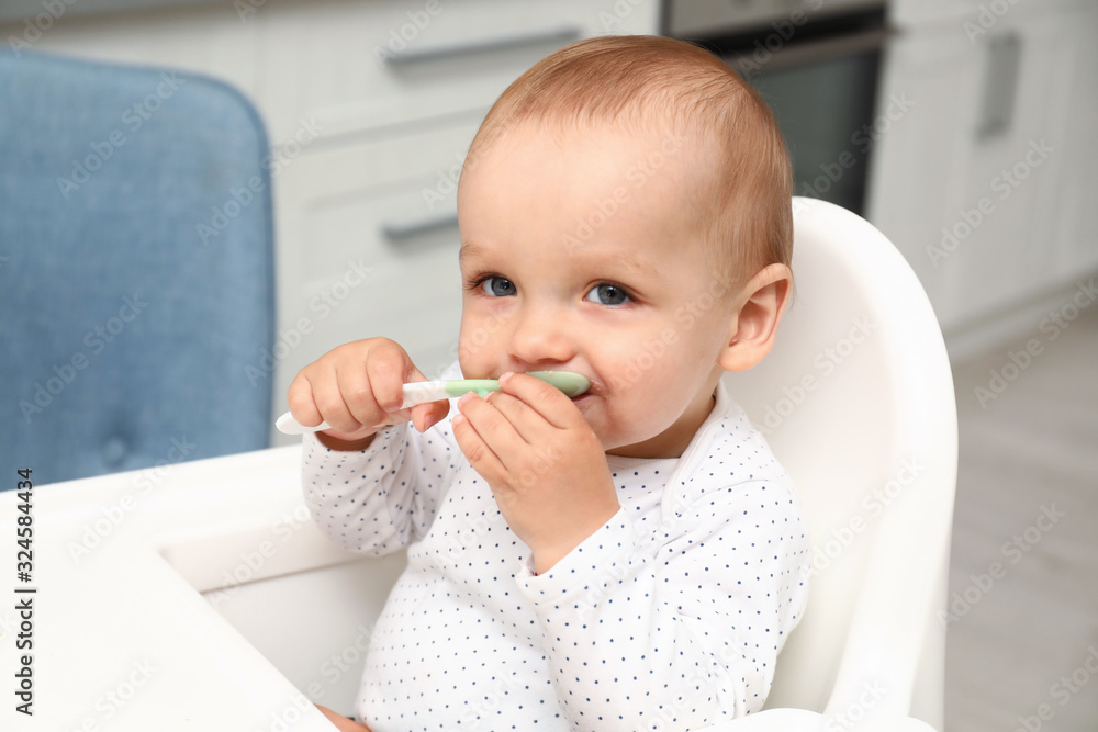 Cute little baby with spoon in highchair at home Cute little baby with spoon in highchair at home