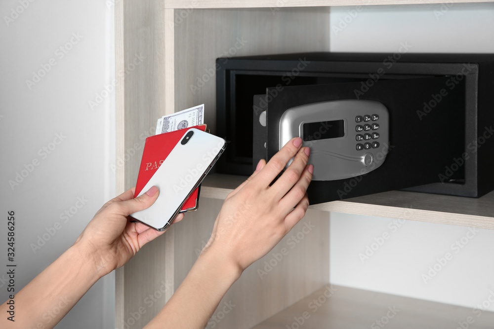 Woman putting smartphone, passport and money into steel safe, closeup Woman putting smartphone, passport and money into steel safe, closeup