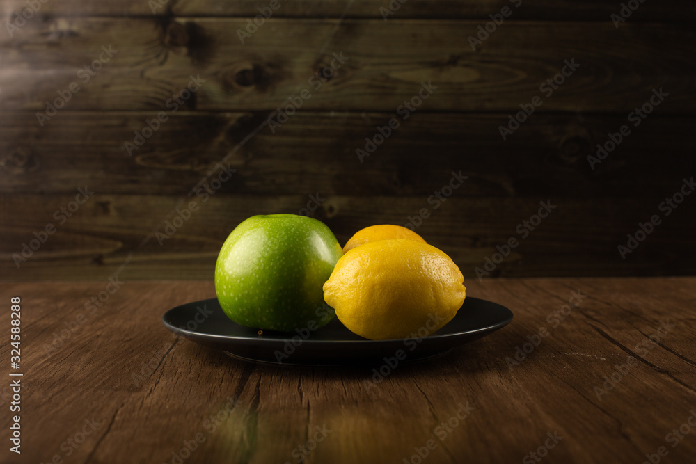 An apple and two lemons in a dark plate.