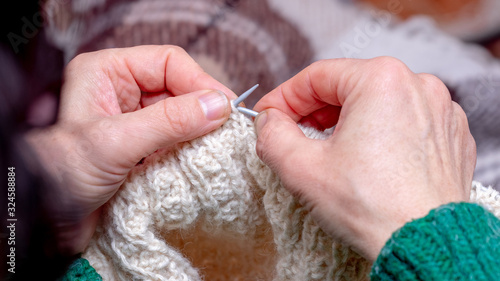 Elderly woman knits a sweater using knitting needles. Handmade_