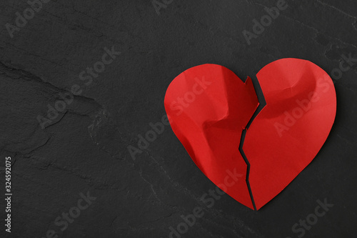 Torn paper heart on black stone background, top view with space for text. Relationship problems concept photo