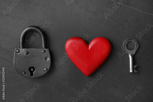 Padlock, wooden heart and key on black stone background, flat lay. Relationship problems concept