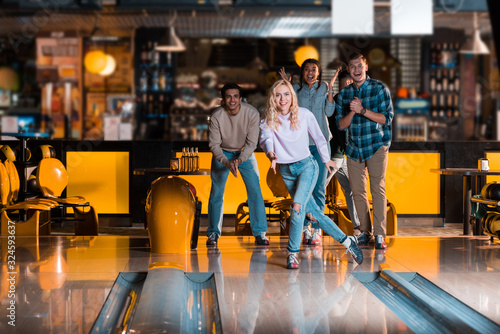 smiling girl looking at skittle alley near excited multicultural friends photo