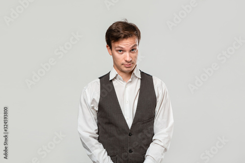 Young man in a white shirt and grey vest in high dudgeon over grey background