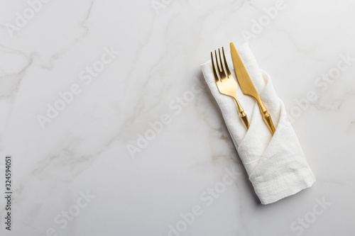 Golden tableware at white napkin on white marble background