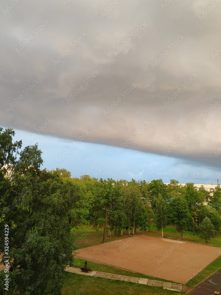 Amazing size huge thundercloud over the park with green trees. Before a rainstorm. Storm warning weather. Amazing size huge thundercloud over the park with green trees. Before a rainstorm. Storm warning weather.