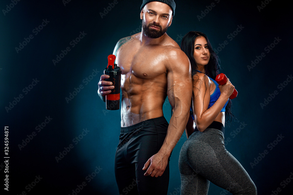 Athletic couple. Man and fit woman with sports equipment on dark background.