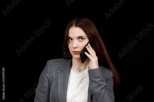 Joyful and successful young fashion blogger is emotionally talking on phone. Beautiful young woman in casual grey jacket is holding smartphone