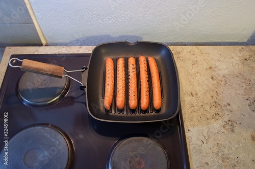 Roast hot dog sausages in a griddle pan on a kitchen burner at home