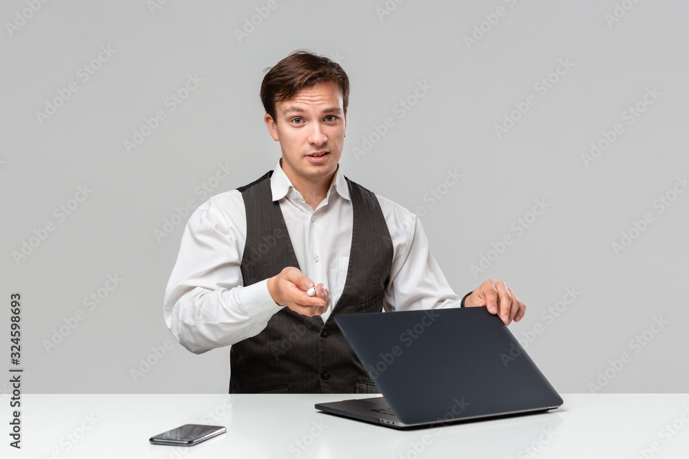 Businessman in a white t-shirt and grey vest working on a laptop. Man looking at the camera Businessman in a white t-shirt and grey vest working on a laptop. Man looking at the camera