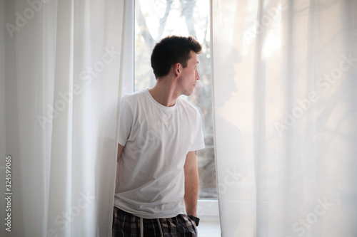 Young man in the white shirt and pajama is relaxing looking at the window