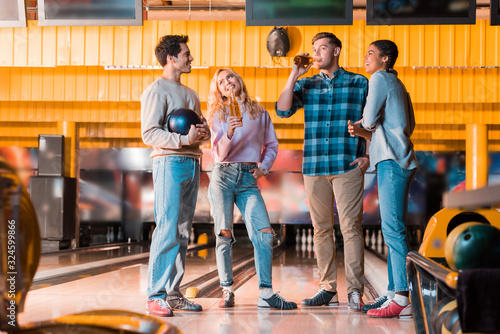 cheerful multicultural friend talking and drinking beer in bowing club photo