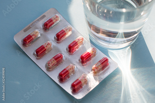 Capsules in blister with water in a clear glass cup on a grey surface. Medicine concept. photo