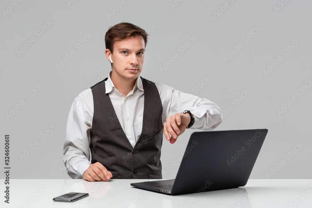 Businessman in a white t-shirt and grey vest looking at wrist watch checking time Businessman in a white t-shirt and grey vest looking at wrist watch checking time