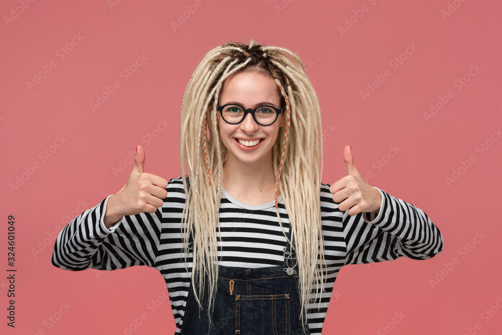 Beautiful young girl with dreadlocks in a striped shirt and jeans jumpsuit  smiling holding thumbs up Stock Photo | Adobe Stock