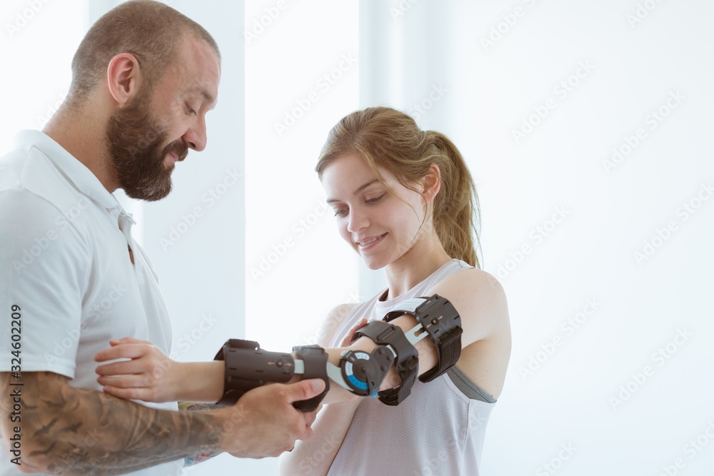 Tattooed physiotherapist who puts an orthosis on the hand of a young patient after an accident Tattooed physiotherapist who puts an orthosis on the hand of a young patient after an accident