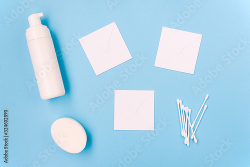 Cosmetic products on a blue background. Facial foam, soap and cotton buds. Three white sheets of paper for text. Body and skin care. Beauty salon, spa concept.