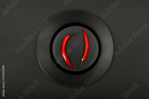 Fresh red hot chili peppers in a black plate on a black background, close-up top view.