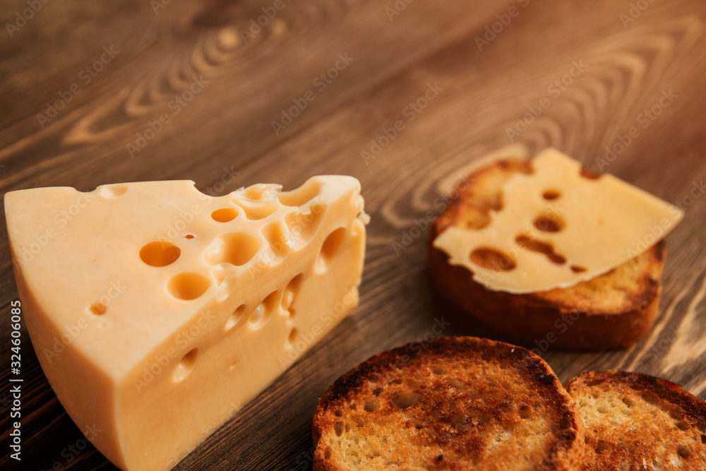 Piece of cheese with large holes and fried bread on a wooden table. Sandwich with cheese.