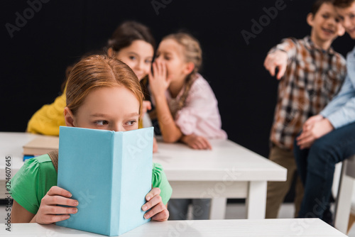 Obraz na plátně selective focus of upset schoolkid covering face with book near classmates gossi