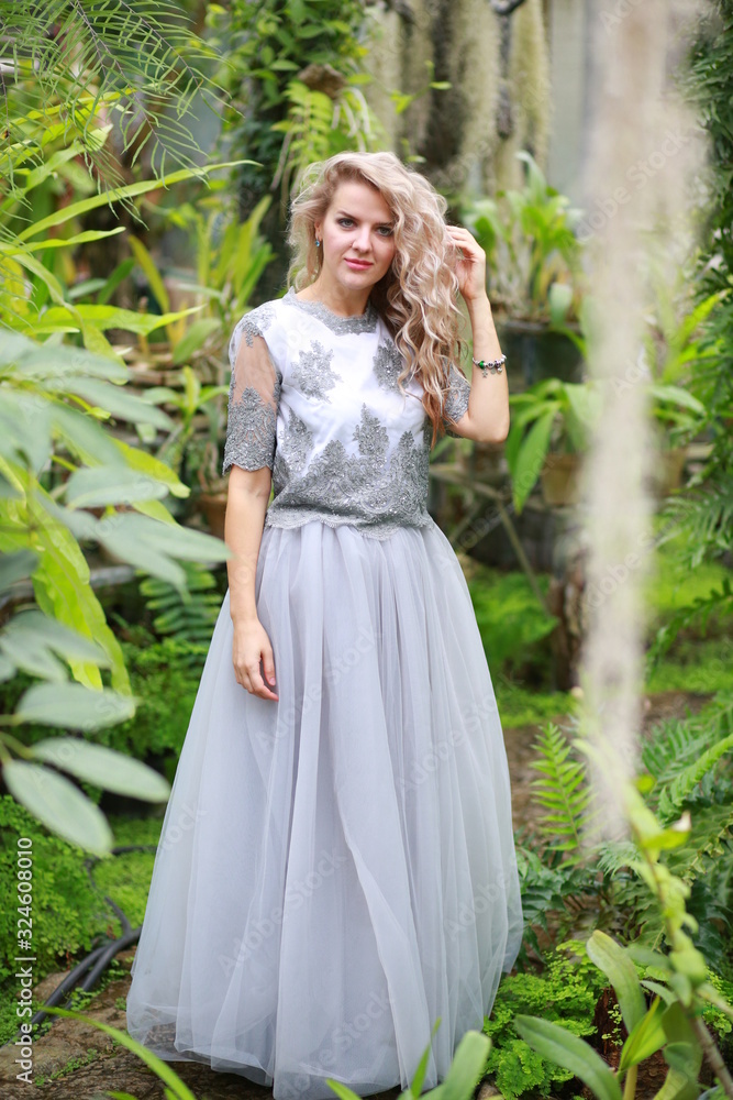beautiful blonde long hair girl in a flying tulle skirt walks in a botanical garden among green plants beautiful blonde long hair girl in a flying tulle skirt walks in a botanical garden among green plants