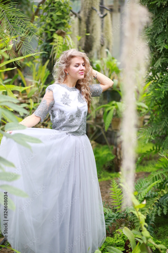 beautiful blonde long hair girl in a flying tulle skirt walks in a botanical garden among green plants beautiful blonde long hair girl in a flying tulle skirt walks in a botanical garden among green plants