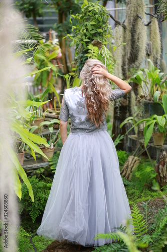  beautiful blonde long hair girl in a flying tulle skirt walks in a botanical garden among green plants