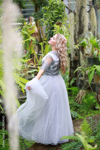 beautiful blonde long hair girl in a flying tulle skirt walks in a botanical garden among green plants