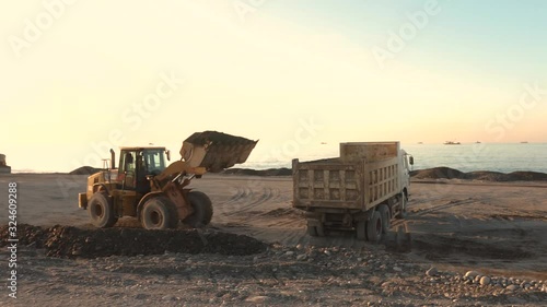 Excavator loads the excavation onto a truck (hydraulic)are heavy construction equipment consisting of an arrow,a bucket and a cabin on a rotating platform.On the beach with the sea and the setting sun