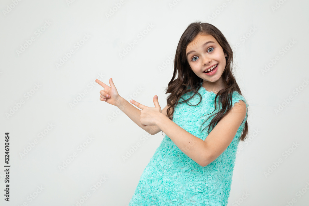 smiling teenage girl in a blue dress points her hands towards empty space on a white studio background smiling teenage girl in a blue dress points her hands towards empty space on a white studio background