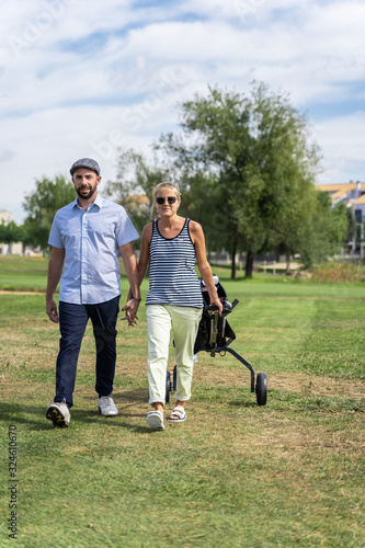 Couple walking hand in hand on a golf course with a cart in the summer