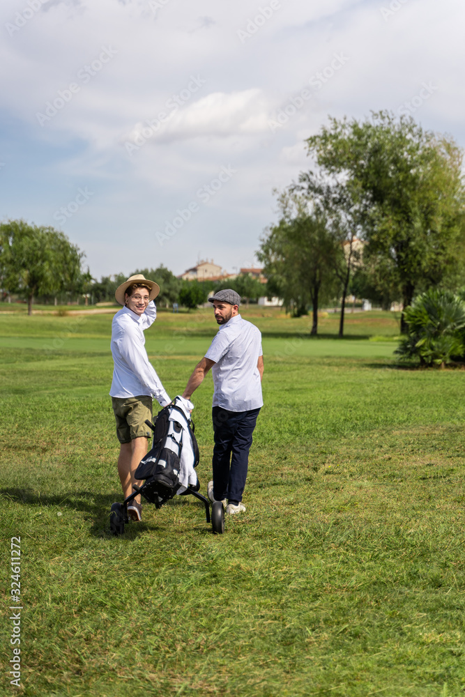 Men walking backwards through a golf course with a cart while turning their heads behind