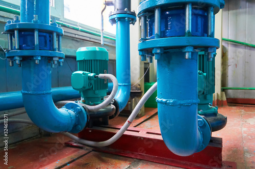 Green vertical motors with pumps on a blue colored water pipeline.