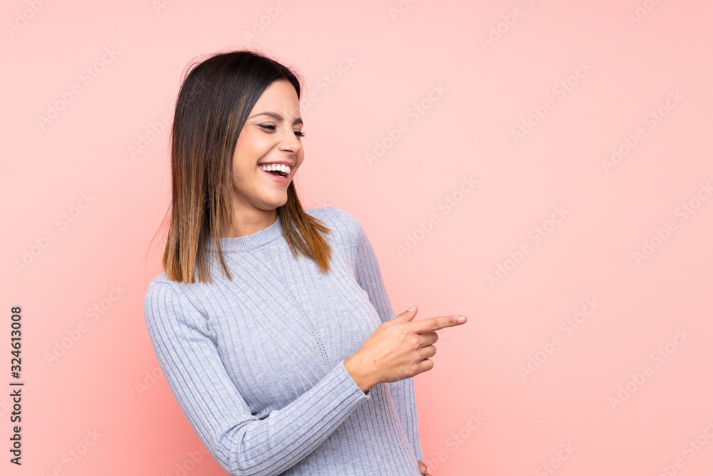 Woman over isolated pink background pointing finger to the side and presenting a product Woman over isolated pink background pointing finger to the side and presenting a product