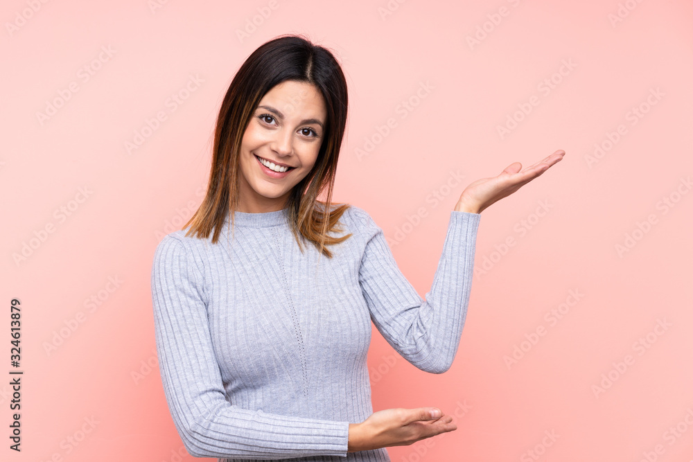 Woman over isolated pink background extending hands to the side for inviting to come Woman over isolated pink background extending hands to the side for inviting to come